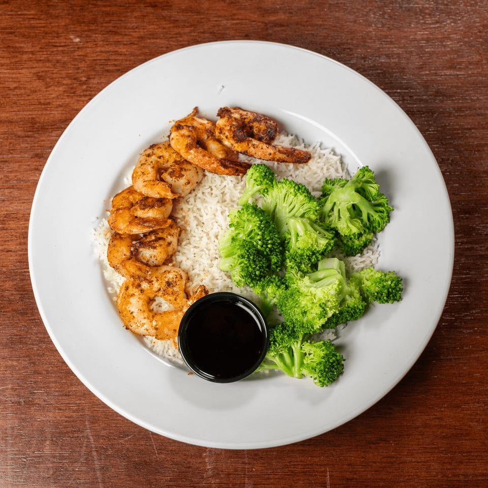 Grilled shrimp, white rice, and broccoli with a side of sauce on a white plate.