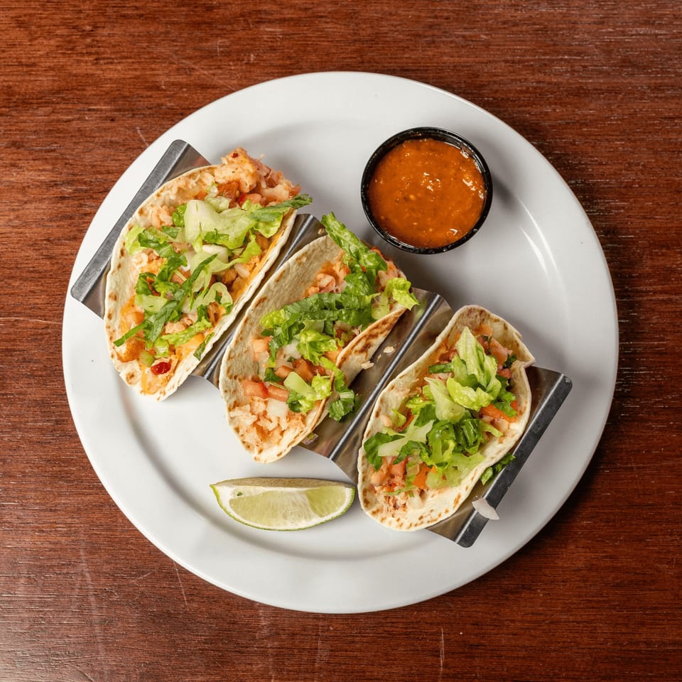 Three Lobster & Beer seafood tacos with lettuce, tomato, and a side of salsa and lime.