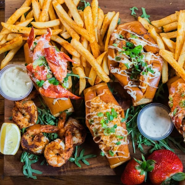 Lobster & Beer NASA seafood platter with lobster rolls, seasoned fries, grilled shrimp, and strawberries.