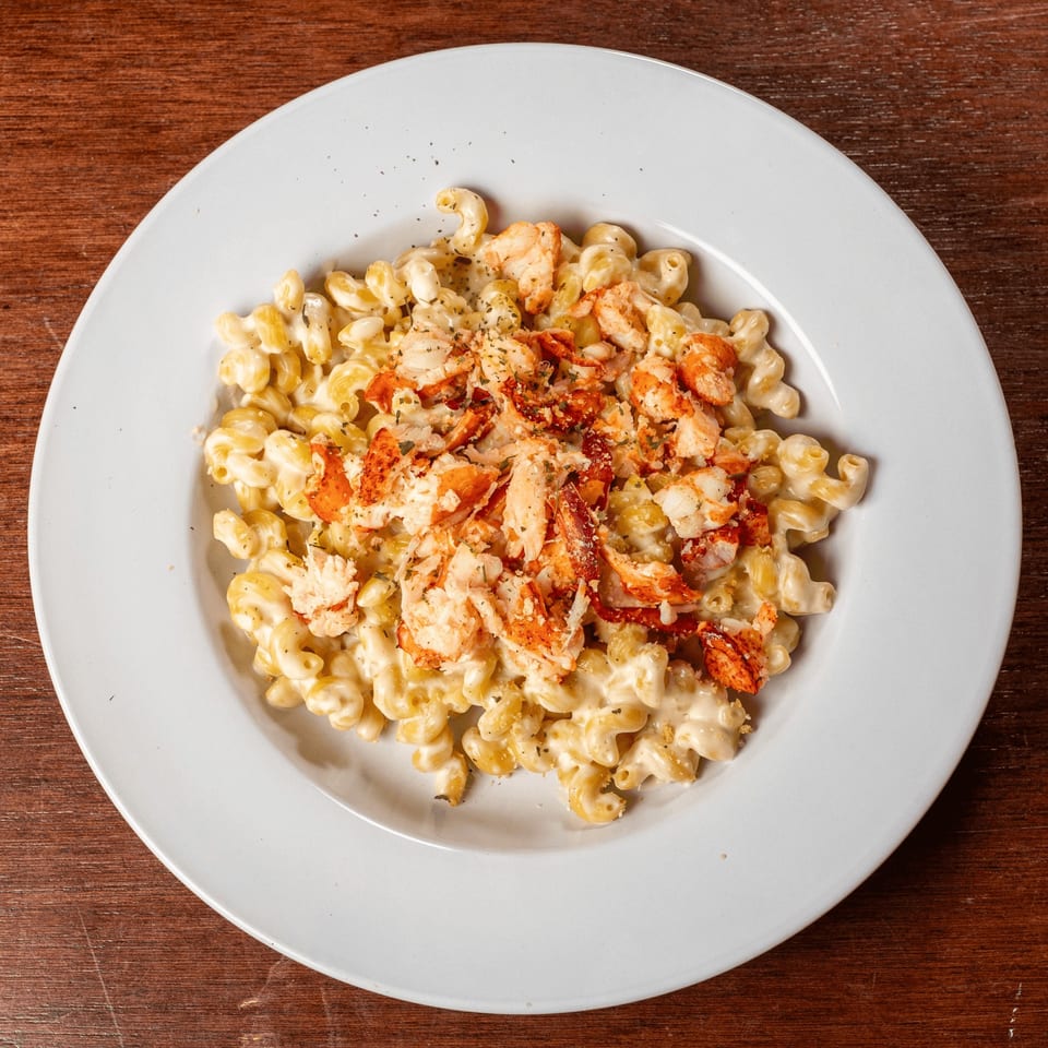 A white plate of creamy macaroni and cheese topped with generous chunks of red lobster meat and herbs.