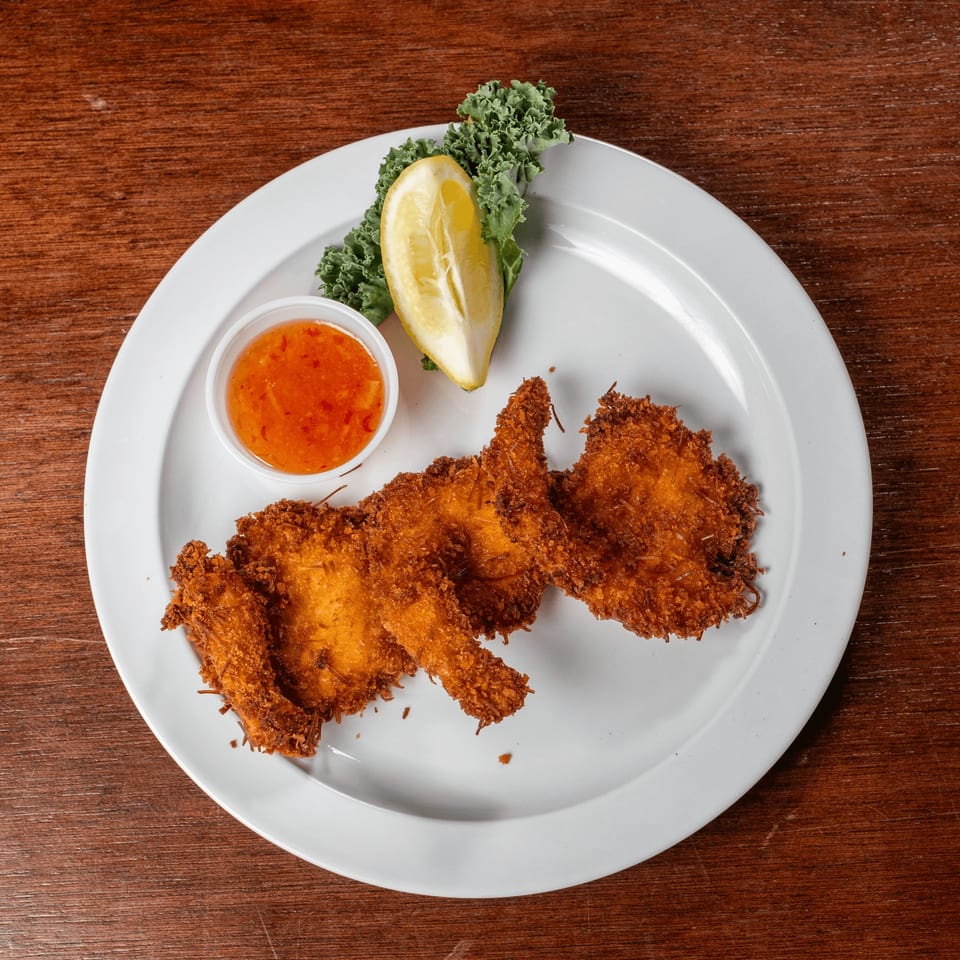 Three pieces of crispy fried coconut shrimp with sweet chili sauce, lemon, and kale on a white plate.