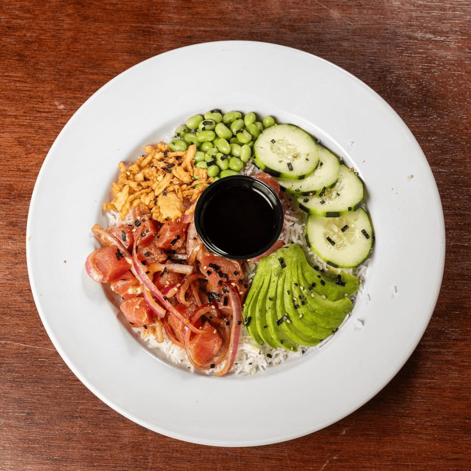 A vibrant poke bowl with tuna, avocado, edamame, cucumber, crispy onions, and sauce on white rice.