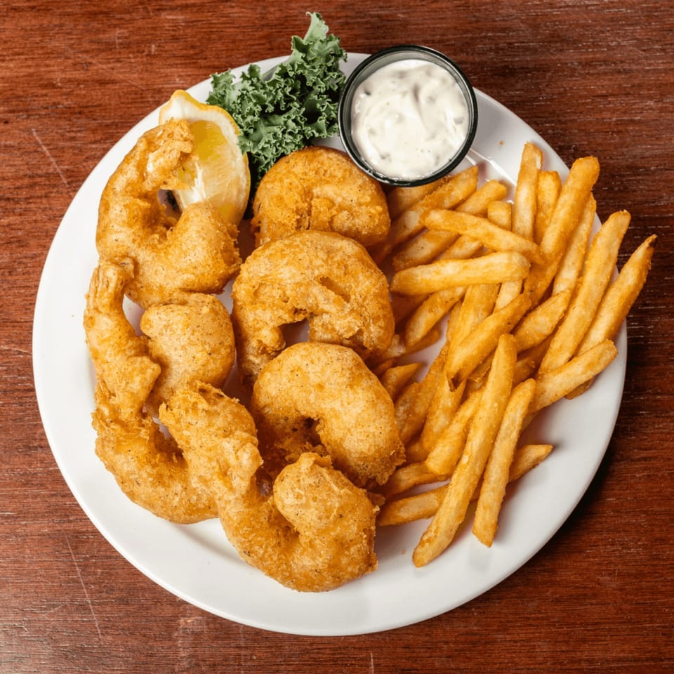 A plate of golden-fried shrimp and french fries with a lemon wedge and tartar sauce.
